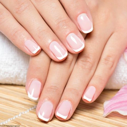 Close-up of hands featuring a French manicure with soft pink and white nails. The setting includes a bamboo mat, white towel, and pink flower petals, evoking a fresh spring vibe.