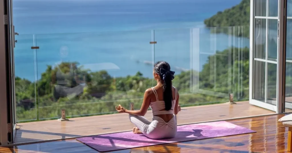 A woman meditating on a purple yoga mat with a stunning ocean view, embracing her glow-up journey in a peaceful and scenic environment.
