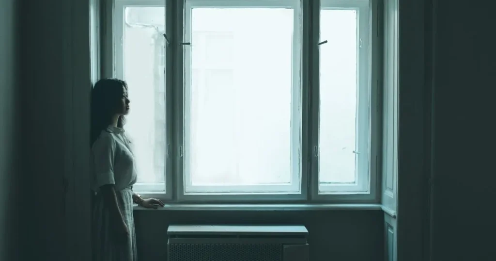 A sad woman lying in bed at night, looking at her phone with a sorrowful expression.